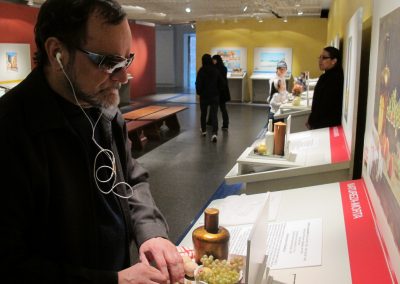 visitante com deficiência visual com fone de ouvido explora maquete tátil na exposição