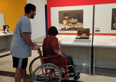 Foto de uma rapaz empurrando uma idosa na cadeira de rodas, eles estão na frente da bancada acessível de Pedro Alexandrino.