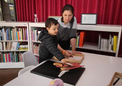 Mulher e criança na mesa de jogos educativos, montando quebra cabeça da obra de Carlos Scliar.