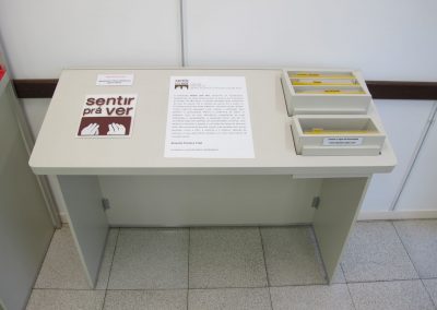 vista superior da bancada de abertura, contendo logotipo da exposição, texto curatorial em dupla leitura e fichas de jogos interativos.
